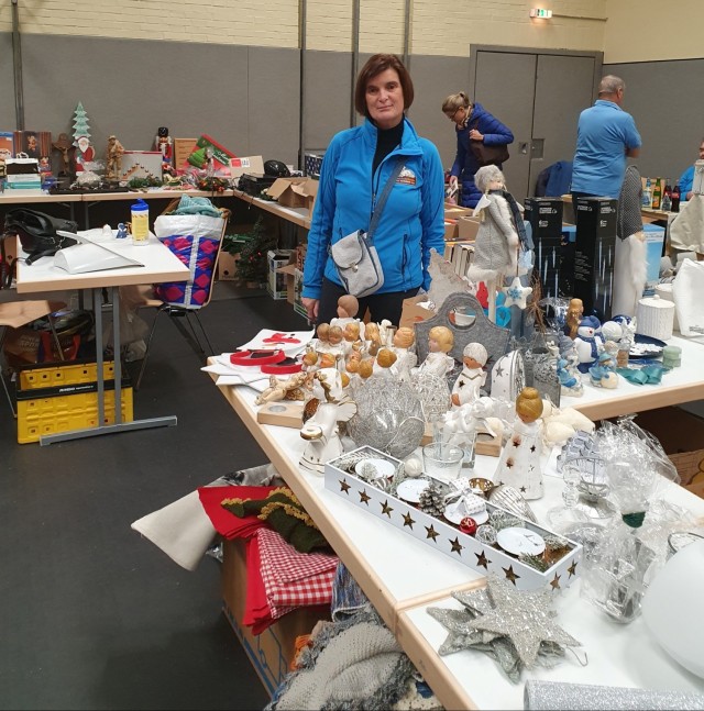 A woman stands next to a table full of items at a rummage sale.