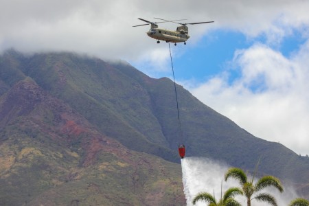 An Army CH-47 Chinook drops seawater over the perimeter of dry land that surrounds the areas impacted by the wildfires in Lahaina, Maui, Aug. 16, 2023. Members of the Hawaii Army and Air National Guard as well as Army active duty and Reserves are supporting Maui County authorities to provide immediate security and safety to those affected by the wildfires.
