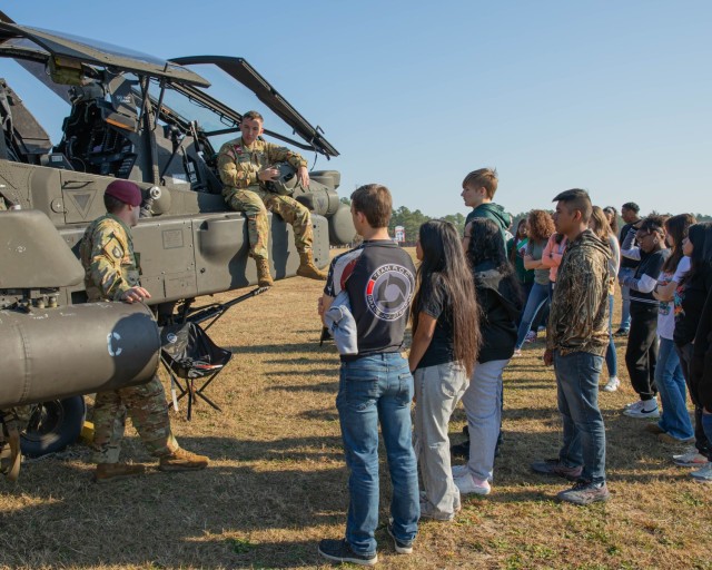 FORT LIBERTY, N.C. — U.S. Army Chief Warrant Officer 2 Frederick O'Connell, left, and Warrant Officer Walter Dumont, right, Apache Helicopter pilots, speak with prospective Soldiers about the various uses of the AH-64 Apache Attack Helicopter during the Meet Your Army Day event at Pike Field on Fort Liberty, N.C., Nov. 8, 2023. The AH-64E program is the most current evolution of the Apache. (U.S. Army photo by Sgt. Omar Joseph)