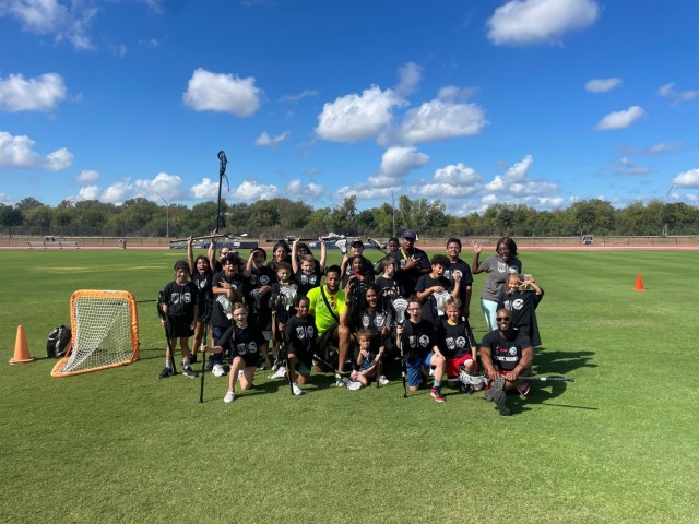 Rick Burton, a patent security specialist for U.S. Army Combat Capabilities Development Command, or DEVCOM, center in bright green, poses for a photo with kids participating in a USA Lacrosse Sankofa Clinic Nov. 4, 2022, in San Antonio, Texas. Burton organizes lacrosse clinics to bring the sport to new communities across the United States. 