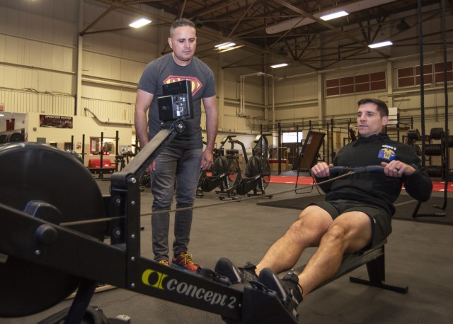 Capt. Brandon Ferraz, Headquarters and Headquarters Company commander, 1st Engineer Brigade, demonstrates some of the capabilities of one of the rowing machines at Cunningham Gym for an attendee at the holistic health and fitness clinic Saturday.