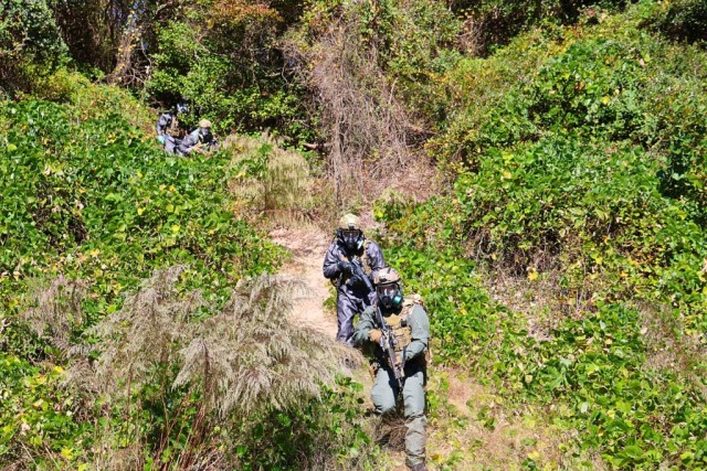 CBRN warfighters wear full protective suit ensembles in an training exercise outside as they walk down a hill