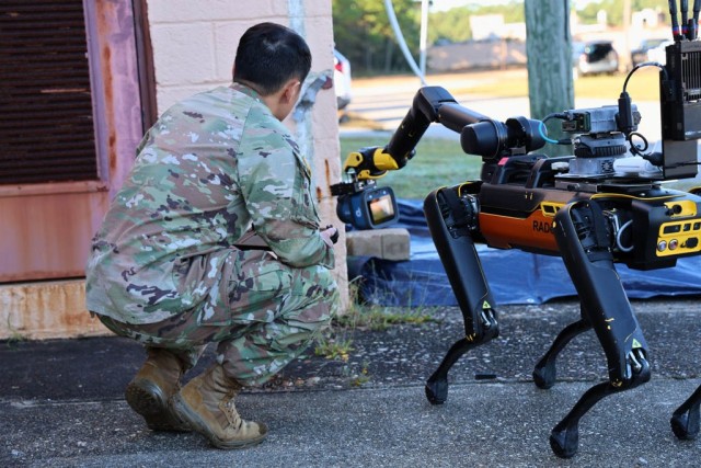 Robotics platforms for CBRN detection and protection, a service member observes as a robot dog uses a CBRN sensor to identify a training specimen