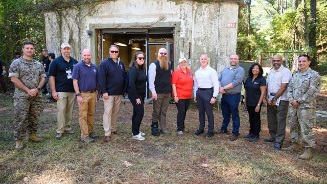 US government leaders and event organizers stand outside in front of a training site.