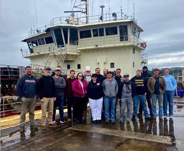 ‘Man Overboard’: Dredge vessel crew saves woman swept away by Columbia River / Alt Text - A group of 16 people stand next to a dredge vessel that is in dry dock. 