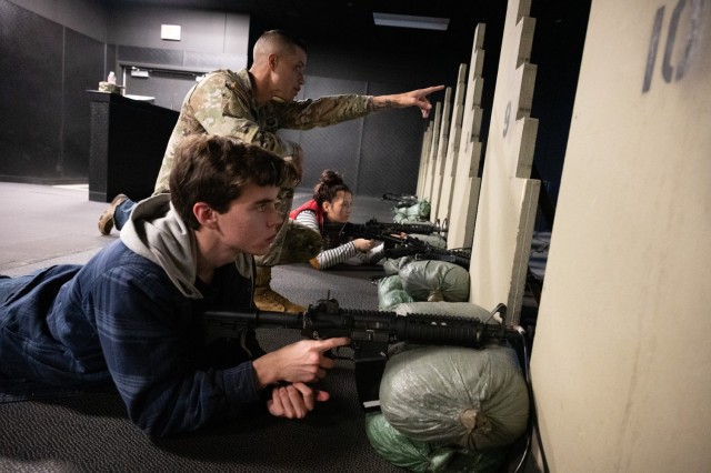 Sgt. 1st Class Garrison Porquez, a drill sergeant for 2nd Battalion, 10th Infantry Regiment, teaches Summersville High School students, Austin Smith and Kyah Rutledge, how to use the M4 rifle Engagement Skills Trainer during their field trip to...