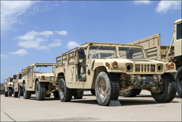 A line of High-Mobility Multi-Purpose Wheeled Vehicles waits for departure in a motor pool