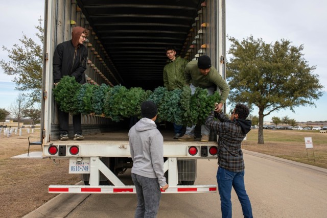 Volunteers lift a pole with 30 wreaths on it into one of the 18-wheeler truck trailers, which is where the wreaths are stored until next holiday season. (U.S. Army photo by Samantha Harms, Fort Cavazos Public Affairs)