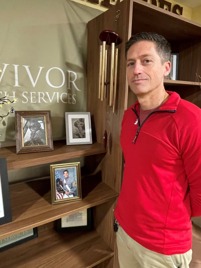 Luca Harbeson stands with a photo of his late father, Chief Warrant Officer 2 James R. Harbeson, who lost his life in a 1990 helicopter crash. The portrait of the late Harbeson is part of the Army Community Service Wall of Heroes.