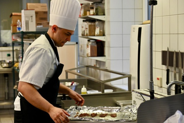 Commissaryman Petty Officer 1st Class John Toman examines a tray of freshly roasted ingredients during a training session of the U.S. Army Culinary Arts Team at the Originals Dining Facility on Panzer Kaserne, U.S. Army Garrison Stuttgart, Jan. 24, 2024.