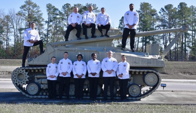 The members of the U.S. Army Culinary Arts Team (USACAT) pose for a group photo. The team consists of: U.S. Army Chief Warrant Officer 4 Karlatta Brown (team manager), Chief Warrant Officer 2 Christine Stanley (team captain), Sgt. 1st Class Andrew Shurden, Staff Sgt. Symone Abreu, Sgt. Nicolas Adame, and Sgt. Marlene Otero; U.S. Navy Petty Officer 3rd Class Larry Burns; U.S. Marine Corps Gunnery Sgt. Michael Watts and Sgt. Jonathan Sanchezbermeo; and U.S. Coast Guard Commissaryman Chief Petty Officer Danielle Hughes and Commissaryman Petty Officer First Class John Toman.