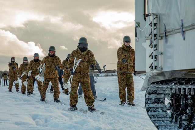 Japanese Ground Self-Defense Force (JGSDF) members with 28th Infantry Regiment, 11th Brigade, Northern Army train give a demonstration on proper technique to ride skis while being dragged by a JGSDF Type 10 Snowcat to U.S. Paratroopers from 1st...