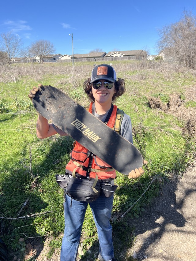 Christopher Richter, a 17-year-old volunteer, shows off a skateboard he found near a stream bed leading into the pond. (U.S. Army photo by Christine Luciano, Fort Cavazos DPW Environmental)