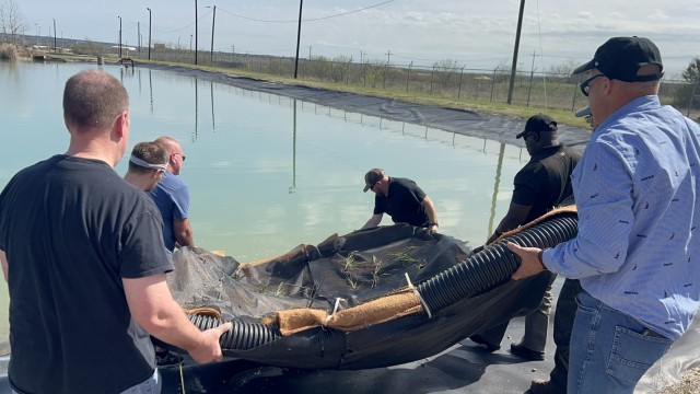 Fort Cavazos Directorate of Plans, Training, Mobilization and Security and Adaptive and Integrative Management Team staff prepare the launch of the U.S.S. Eddy, a prototype floating island, off the shore of a catchment basin in the North Fort Cavazos tactical vehicle wash facility. (U.S. Army photo by Christine Luciano, Fort Cavazos DPW Environmental)