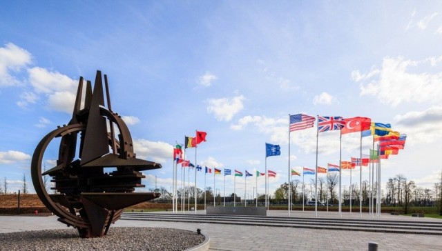 The NATO star sculpture in the foreground and the country flags of NATO in the background. 