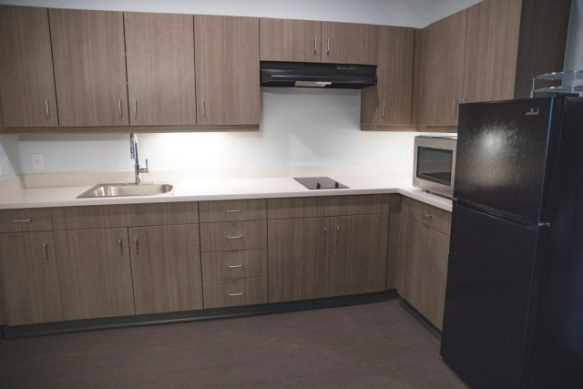 A kitchen with wooden cabinets, an electrice stove, a silver microwave and a black refrigerator. 