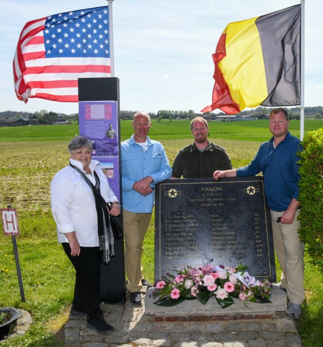 A family stands next to a plaque with the US and Belgian flag in the background. 