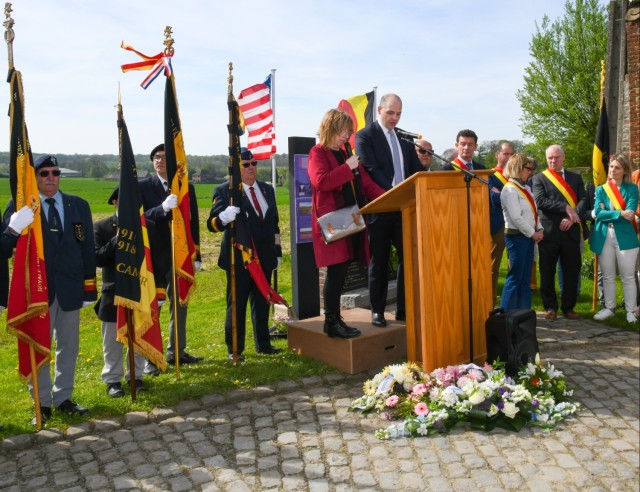 Two people talking on a stage during commemorative events with others in the background. 