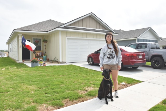 A woman and her black Labrador retriever pose for a photo on a sidewalk in a front of a single family home. 