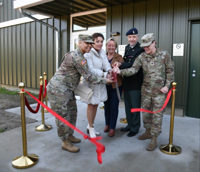 Five individuals holding giant red scissors right after cutting a red ribbon for the grand opening.  