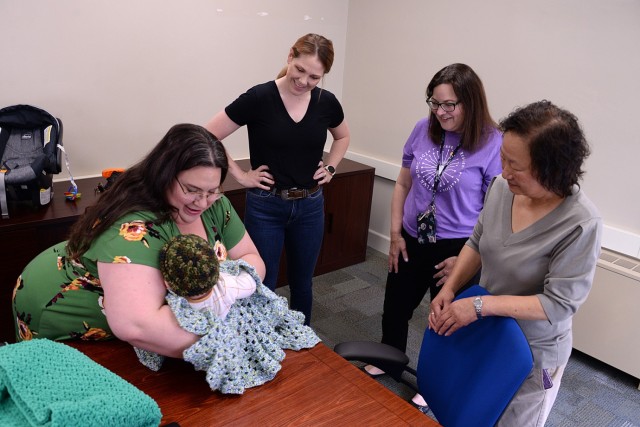 Volunteer Laura Benner demonstrates how to swaddle a newborn in one of her crocheted creations using Jennifer Garrett’s 5-month-old son John as a model as Garrett; Amy McCauley, child and family specialist with the New Parent Support Program;...