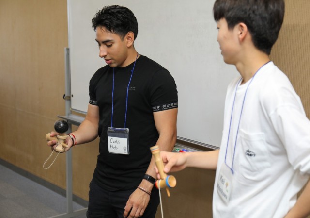 Spc. Carlos Melo, left, assigned to the 38th Air Defense Artillery Brigade, practices the kendama game with a Japanese student during a language and cultural event at Zama City Hall, Japan, May 3, 2024. The volunteers helped a group of students...