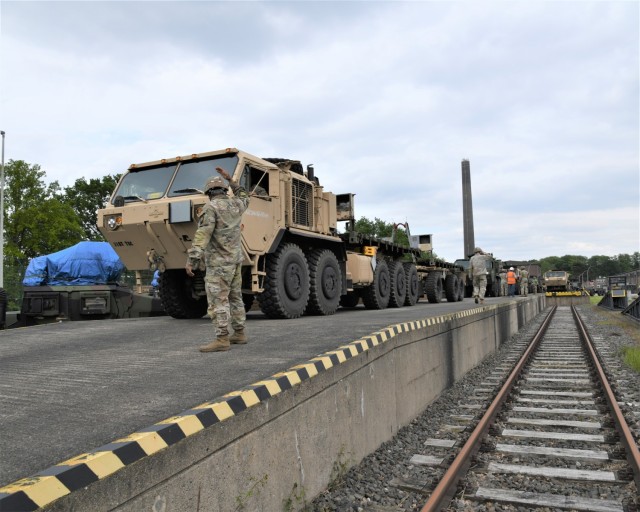 A U.S. Soldier directs a convoy of military vehicles next to railroad tracks.