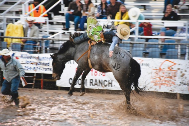 A man sits on a horse bucking in the mud