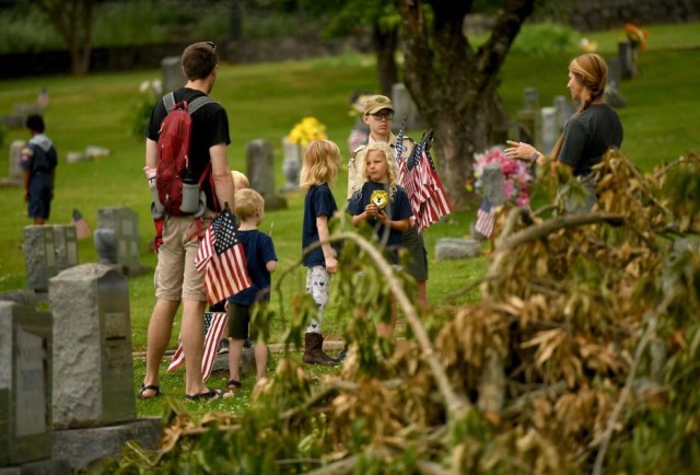 Andrew and Karen Herron, of Huntsville, lead their kids, Simon, Lawrence, Miranda, Oliver and Hazel, through the fallen trees to post American flags on the graves of the veterans buried at Maple Hill Cemetery on Saturday.