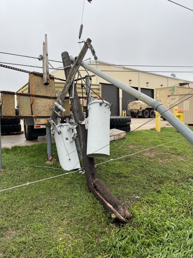 An electric pole lays on a patch of grass, it&#39;s wood snapped, broken and bent, the metal items attached to also in similar conditions.