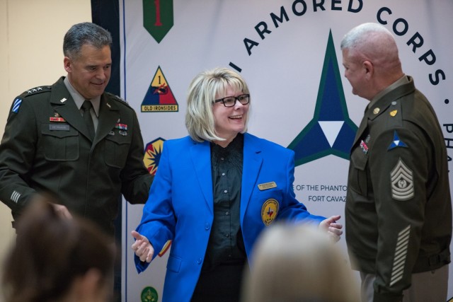 A woman stands smile at a man standing left of her while another man to the right of her looks on.
