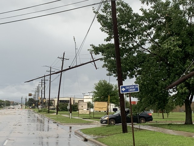 A row of electrical poles stand, one hanging up in the air horizontally. A street lays wet with wooden debris scattered along it.