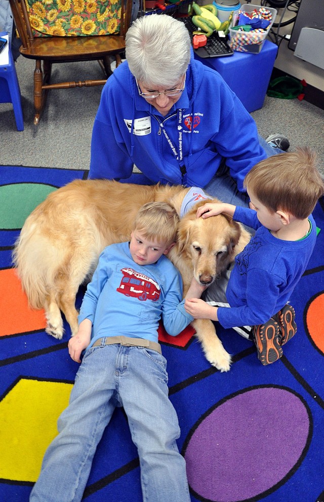 Fort Leavenworth Human Animal Bond member Joanie Linn visits with students in the early childhood special education class as 4-year-old Cayden Hoad snuggles into Linn's golden retriever, Abby, and 4-year-old William Gerling pets the dog's head...