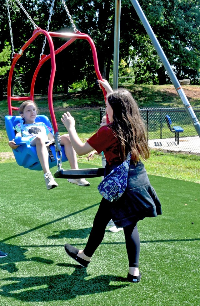 Madison Maxwell, 10, daughter of 1st Sgt. John Maxwell, 502nd Engineer Battalion, and Molly Griggs, 10, daughter of Maj. Charles Griggs, 1st Army Division, demonstrate how to use a swing designed for special needs and mobility impaired children at the new inclusive playground on Fort Knox, Kentucky, July 18, 2024.