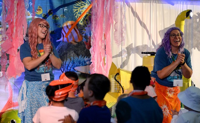 Volunteer song and dance leaders Amy Quinlan and Jamie Showers, portraying mermaids Coral and Opal, teach actions to correspond with the words to songs to Vacation Bible School participants Aug. 6, 2024, at Frontier Chapel on Fort Leavenworth,...