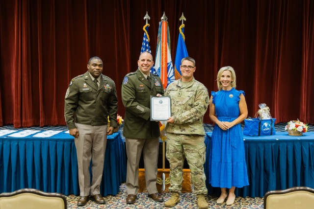 Col. John P. Miller III, Fort Novosel garrison commander, Fort Novosel garrison Command Sgt. Maj. Garry Williams, and Mrs. Mollie Miller present Spc. Dakota Lowry Rapley with a volunteer award at The Landing on Aug. 27, 2024.