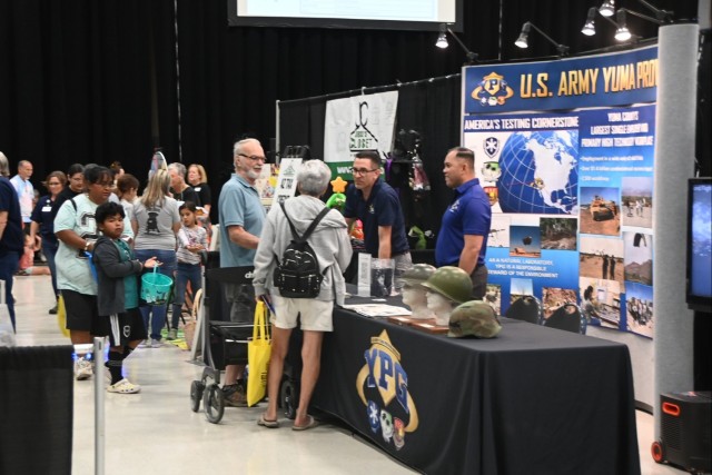 U.S. Army Yuma Proving Ground (YPG) Public Affairs Officer Mark Schauer (left, at table) and Command Sgt. Maj. Mark Millare (right, at table) engage with eventgoers at the heavily attended Yuma Community Expo on October 19, 2024. YPG&#39;s...