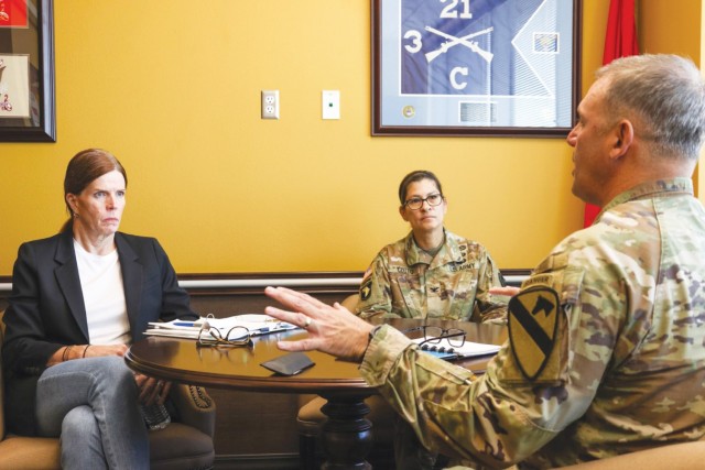 A man sits across a round table from two women while he talks, and the women look on. 