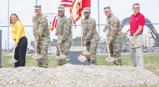 A group of people pose for a picture behind a mound a gravel while standing and holding shovels holding gravel.