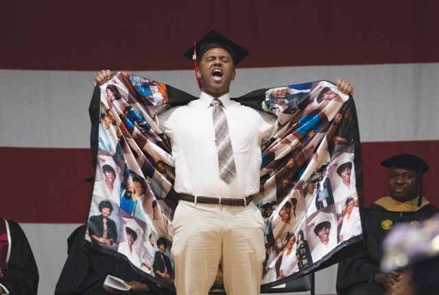 A man standing holds open his graduation gown, showing a collage of photos on the inside fabric.