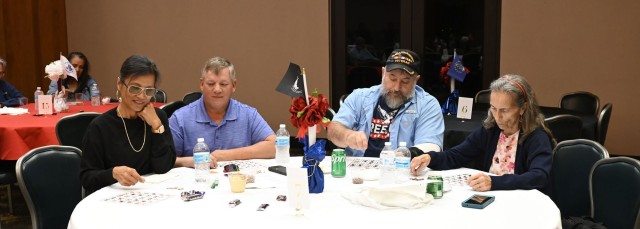 Four people sitting at a table look down at bingo cards resting on the table. 