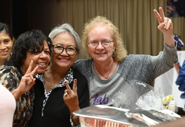 Three women standing pose for a picture while throwing peace signs. 