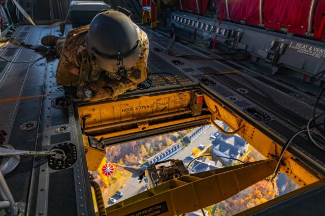 Connecticut Army National Guard Sgt. Adam Osip, a CH-47 helicopter repairer assigned to the 2nd Battalion, 104th Aviation Regiment, looks through the center cargo hook hatch of a CH-47F Chinook transport helicopter as it sling loads a helicopter...