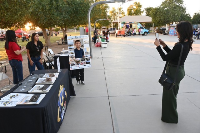 U.S. Army Yuma Proving Ground Public Affairs Specialist Ana Henderson (left) helps a delighted youngster appear on the front cover of an oversized cut-out of the post newspaper, The Outpost, at the first annual Mesquite Elementary School Community...