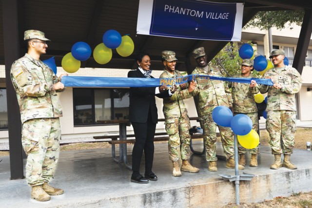 Six people standing hold on to a long, blue ribbon while the man standing left center holds the ribbon between a pair of scissors. 