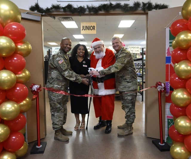 Four people standing pose behind a ribbon tied between two poles, holding a giant pair of scissors poised to cut the ribbon.