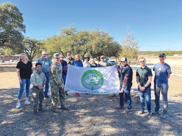 A group of people standing pose for photo, two of the people holding a large white banner between them that reads &#34;TREE CITY USA&#34; with a drawn tree.