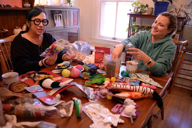 อาสาสมัครของ Fort Leavenworth Stray Facility Marisa Ranney และ Jennifer Johnston เติมขนมและของเล่นแมวลงในเครื่องประดับใสเพื่อวางไว้บนพวงหรีดธีมสุนัขและแมวในวันที่ 21 พฤศจิกายน 2024 ที่บ้านของเพื่อนอาสาสมัครที่ Fort Leavenworth รัฐแคนซัส ที่...