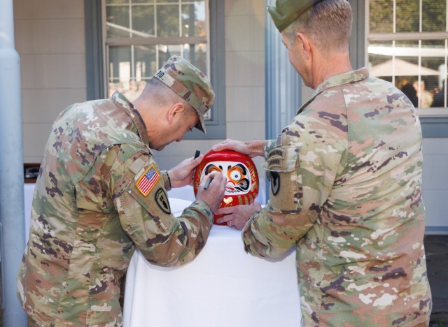 Col. Marcus Hunter, right, commander of U.S. Army Garrison Japan, watches Command Sgt. Maj. David A. Rio paint in the second eye of his &#34;daruma&#34; doll before a change of responsibility ceremony at Camp Zama, Japan, Dec. 12, 2024. Command Sgt. Maj. Rick Meeker assumed responsibility of the garrison&#39;s senior enlisted leader role from Rio, who plans to take a position at Fort Gregg-Adams, Virginia.