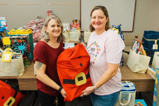 Jo Close, Army Community Service AER officer and Angel Tree coordinator, hands a gift to volunteer Ginny Fricks, Fort Novosel Thrift Shop Chairmen of the Board of Directors, during the distribution of gifts for the 2024 Angel Tree project Dec. 19.